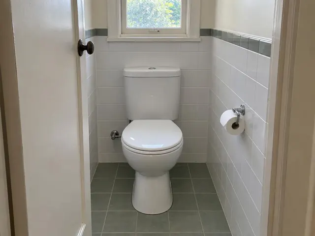 Clean white toilet in a small tiled bathroom with a window and toilet roll holder in Hornsby