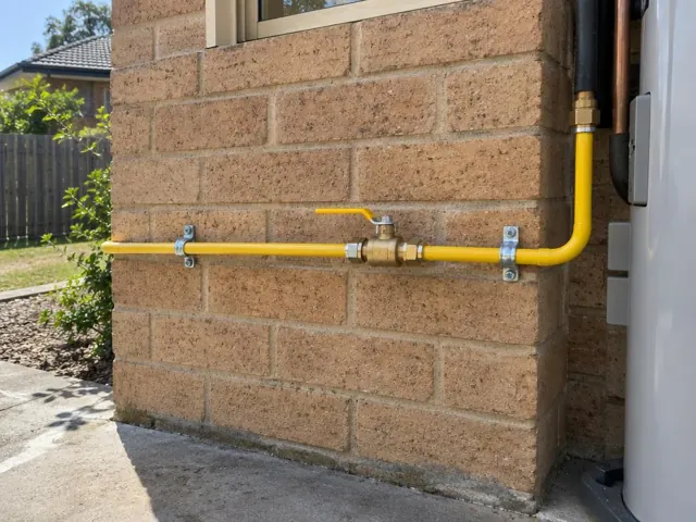 Yellow gas pipe and valve on a brick exterior wall beside a house in Mount Colah