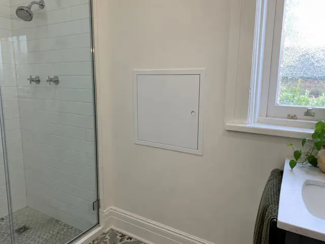 Small access panel in a painted bathroom wall beside a shower and window in Asquith