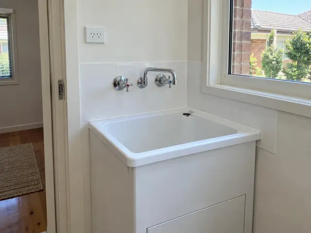 New wall tap above a white laundry tub beside a window and tiled wall in Waitara